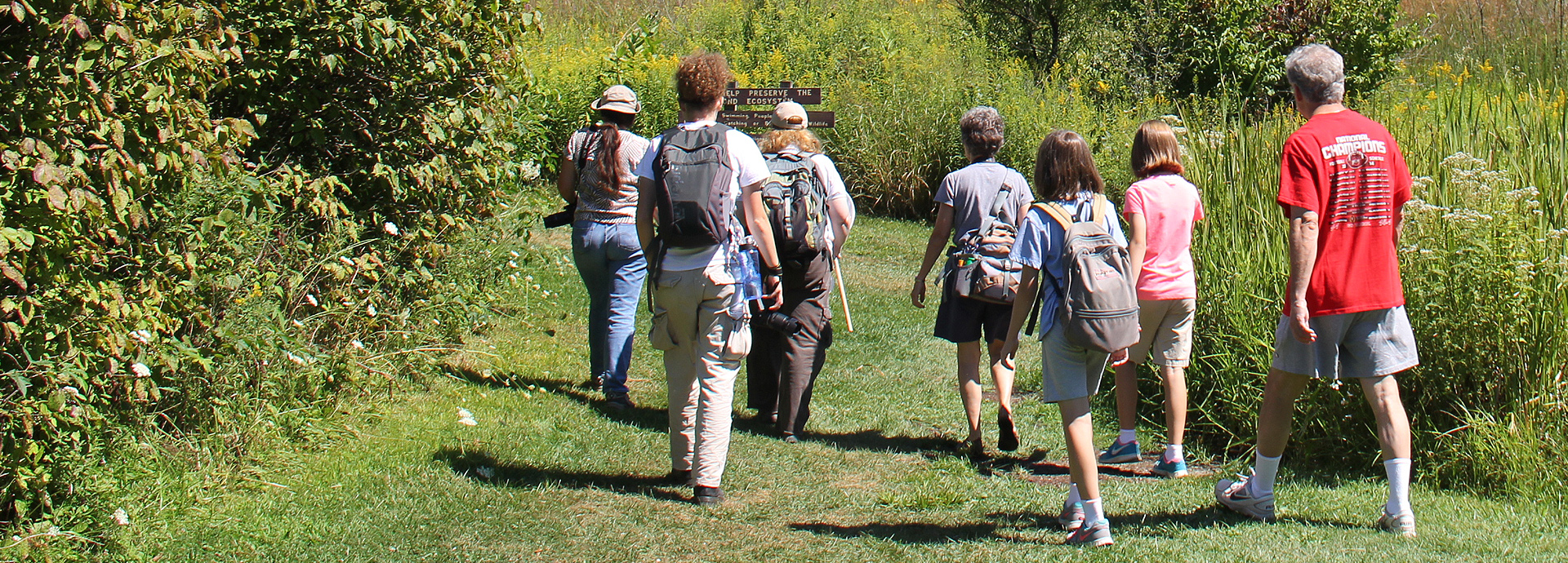Slideshow Image - A group of people hiking through GNC's prairie