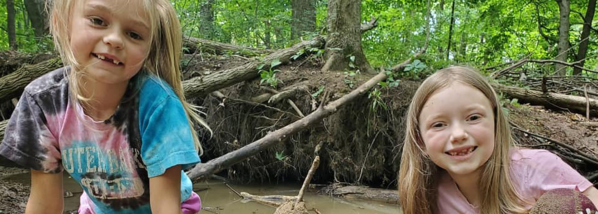 Slideshow Image - Two young girls standing beside a large tree next to GNC's stream