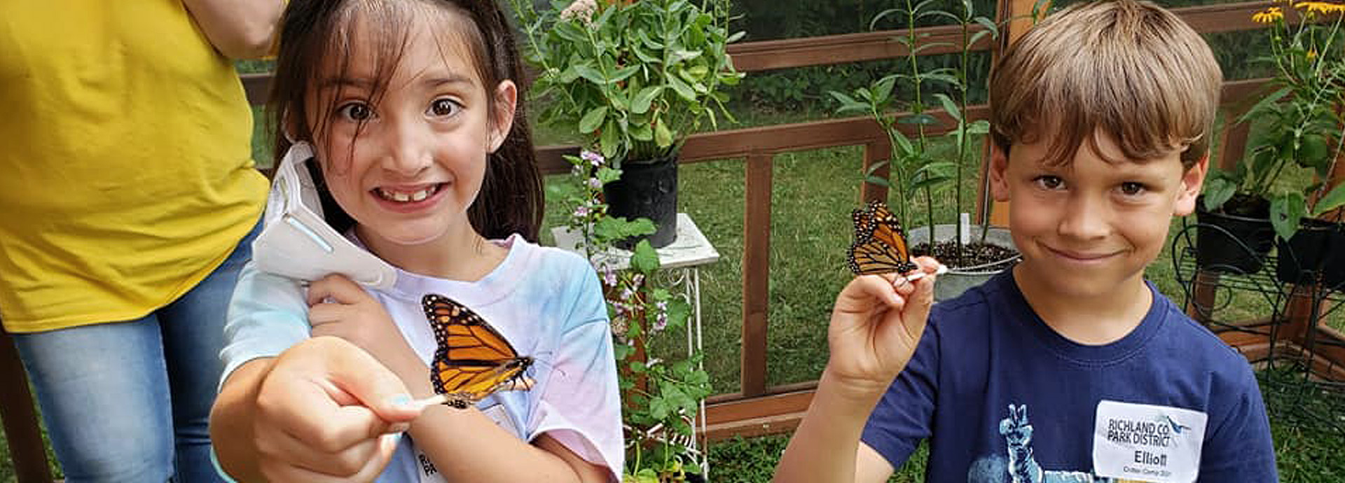 Slideshow Image - Two young children feeding Monarch butterflies